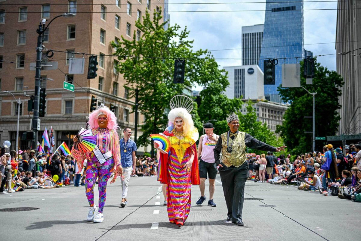 Three members of Pride royalty marching through the street